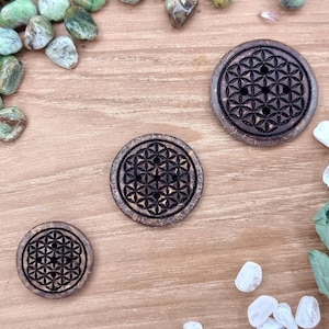 Könnte beinhalten: Drei Untersetzer aus Holz mit einem Lebensblume-Design. Die Untersetzer sind braun und haben eine natürliche Holzoptik.