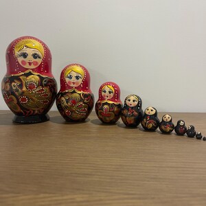 K&ouml;nnte beinhalten: Eine Reihe traditioneller russischer Matrjoschka-Puppen. Die Puppen sind in Rot, Schwarz und Gold bemalt und weisen Blumen- und Vogelmuster auf. Die gr&ouml;&szlig;te Puppe ist etwa 15 cm hoch.