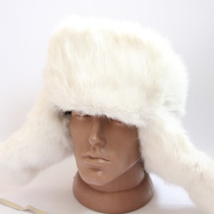 May include: A white fur hat with ear flaps. The hat is made of soft, fluffy fur and has a classic, warm look.