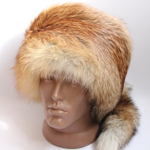 May include: A luxurious, fur hat in shades of brown and tan, displayed on a mannequin head. The hat features a rounded crown and a long, fluffy tail. The fur appears soft and dense, suggesting warmth and quality.
