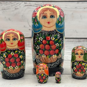 Könnte beinhalten: Ein Set aus sechs russischen Matrjoschka-Puppen, jede bemalt mit einem Frauengesicht und floralen Designs. Die Puppen sind hauptsächlich rot, schwarz und grün, mit goldenen Akzenten. Die größte Puppe ist etwa 18 cm hoch.