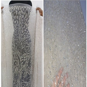 May include: White sheer fabric with silver glitter embellishments. The fabric has a pattern of silver glitter lines and a small silver glitter animal design. The fabric is labeled "TUCF The Urban Couture Factory".