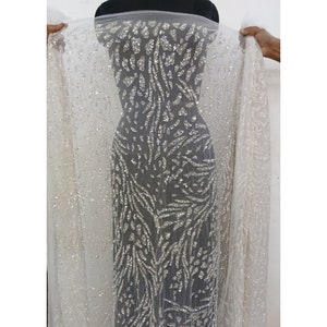 May include: White sheer fabric with silver glitter and a silver leaf pattern. The fabric is draped over a mannequin. The text "TUCF The Urban Couture Factory" is printed at the bottom of the image.