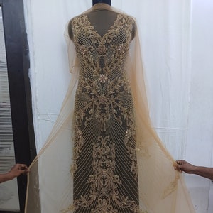 May include: A gold beaded and sequined fabric with a sheer overlay. The fabric has a floral pattern and is designed for a dress or gown.