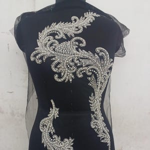 May include: A silver beaded applique with a floral design. The applique is on a black background.