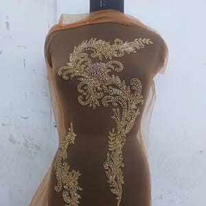 May include: Gold beaded applique with a floral design on a brown mesh fabric.