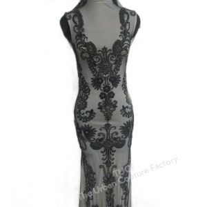 May include: A black beaded embellishment on a sheer fabric, resembling a dress. The embellishment features a floral design with intricate details. The text "The Urban Couture Factory" is visible in the lower right corner.