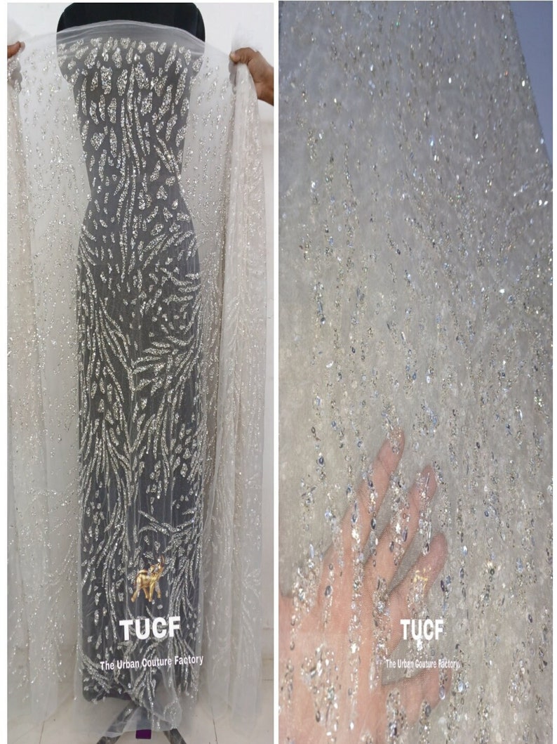 May include: White sheer fabric with silver glitter embellishments. The fabric has a pattern of silver glitter lines and a small silver glitter animal design. The fabric is labeled "TUCF The Urban Couture Factory".