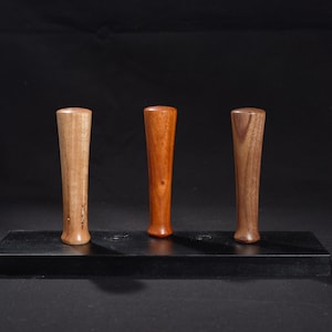 Puede incluir: Tres tapones de botella de madera en diferentes tonos de marrón, expuestos sobre una superficie negra.