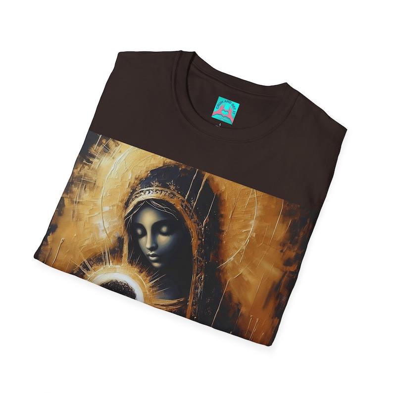 May include: A dark brown t-shirt featuring a printed graphic of a figure with closed eyes wearing a head covering, rendered in shades of gold and black with a radiant halo effect. The inner neck label displays the text "COME AND GET IT".