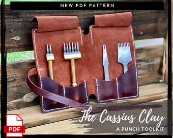 May include: A brown leather pouch with a white stitching detail, containing a set of leather working tools. The pouch has a strap and is labeled "The Cassius Clay A PUNCH TOOLKIT".