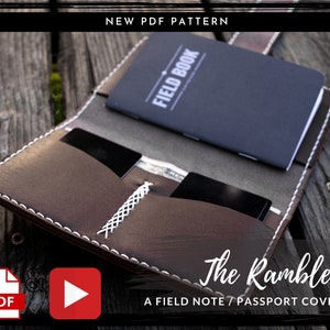 May include: A brown leather passport or field note cover with white stitching. The cover has a flap with a strap and a pocket for cards. The text "The Rambler" and "A FIELD NOTE / PASSPORT COVER" is printed on the cover.