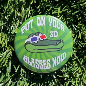 May include: A green button with a white swirl pattern and the text "Put on your 3D glasses now". A cartoon alligator wearing 3D glasses is in the centre of the button.