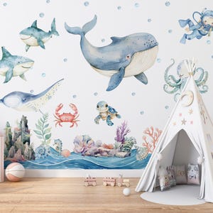 May include: Watercolor wall decals featuring marine life, including sharks, a whale, a manta ray, and a crab. The design includes a coral reef, a diver, and a teepee tent, creating a whimsical underwater theme for a child's room.