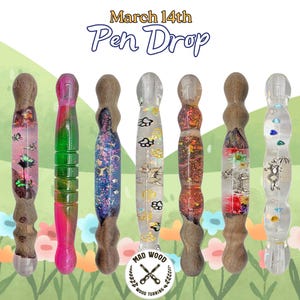 Może przedstawiać: Siedem ręcznie wykonanych długopisów o unikalnych wzorach. Długopisy mają kolorowe żywiczne korpusy z wbudowanymi elementami, takimi jak brokat, kwiaty i małe figurki. Obraz zawiera tekst "March 14th Pen Drop" i logo Mad Wood Turning.