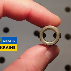 May include: A small, metallic ring with two screws, held between fingers. The ring has a circular shape with a central opening. The image includes a "MADE IN UKRAINE" sticker with the Ukrainian coat of arms.