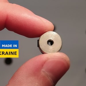 May include: A small, silver-colored metal component with a square hole in the center. The component is held between fingers. A sticker in the image reads "MADE IN UKRAINE" with the Ukrainian flag.