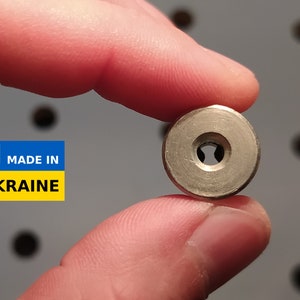 May include: A silver metal disc with a small hole in the center. The disc is being held by a hand. The text "MADE IN UKRAINE" is visible in the background.