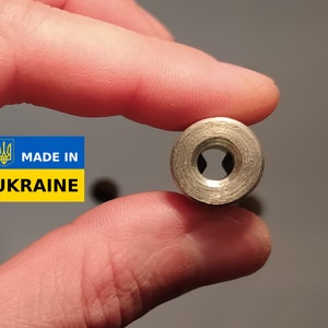 May include: Close-up of a silver metal nut with a hexagonal shape and a threaded hole in the center. The nut is held in a hand, and the background is a light gray surface. The text "MADE IN UKRAINE" is visible in the lower left corner of the image.