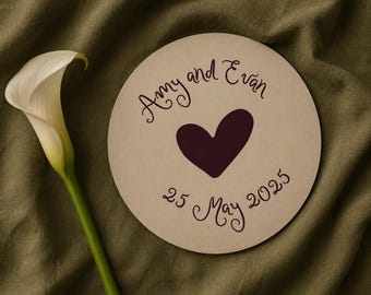May include: A beige circular wedding announcement with the names "Amy and Evan", a dark purple heart, and the date "25 May 2025". A white calla lily with a green stem is on the left.