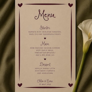 Può includere: Un menu rettangolare in carta con sfondo color crema e testo bordeaux scuro. Il menu presenta un bordo con icone a forma di cuore in ogni angolo, elencando portate come burrata, pollo arrosto e panna cotta per Chloe & Evan.