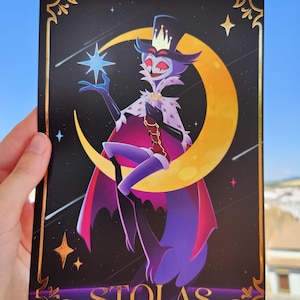 May include: A postcard featuring a cartoon character with a crown, cape, and top hat, holding a blue star against a crescent moon. The background is black with stars and shooting stars. The word "STOLAS" is at the bottom, with a gold border.