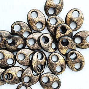 May include: A group of oval-shaped beads with two holes each. The beads are black with a gold metallic finish.