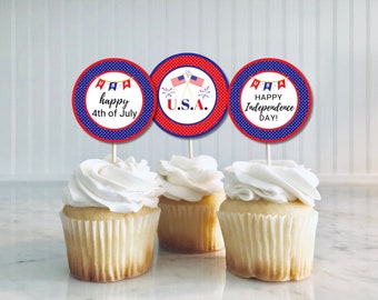 May include: Three red, white, and blue cupcake toppers with a polka dot background. The toppers feature the text "U.S.A." and "Happy Independence Day!" and "happy 4th of July". The toppers are on top of cupcakes with white frosting.