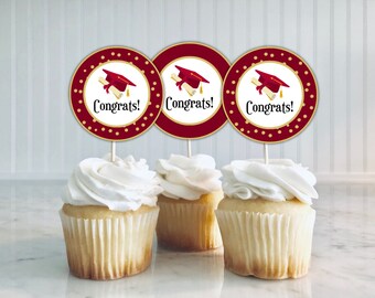 Pode incluir: Três toppers para cupcake vermelhos e dourados com um design de chapéu de formatura e diploma. Os toppers dizem "Parabéns!" em letras douradas.