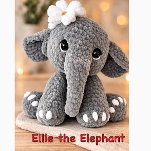May include: A gray crocheted elephant plush toy with a white flower on its head. The elephant has large black eyes and white accents on its feet. The text "Ellie the Elephant" is displayed in red at the bottom.