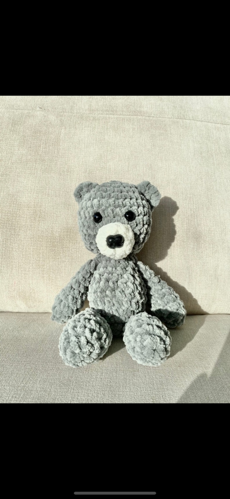 Puede incluir: Un oso de peluche gris tejido a crochet con detalles blancos alrededor de la nariz y la boca. El oso est&aacute; sentado sobre una superficie texturizada gris claro.