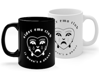 May include: Two ceramic mugs with black and white designs. The black mug has white text that reads "elder emo club it wasn't a phase". The white mug has black text that reads "elder emo club it wasn't a phase". Both mugs feature a black and white illustration of a heart with a crying face.