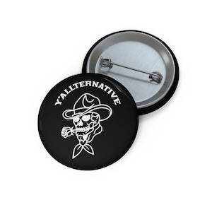 May include: A black and white button with a skull wearing a cowboy hat and smoking a rose. The text "Y'ALLTERNATIVE" is written in white around the skull.