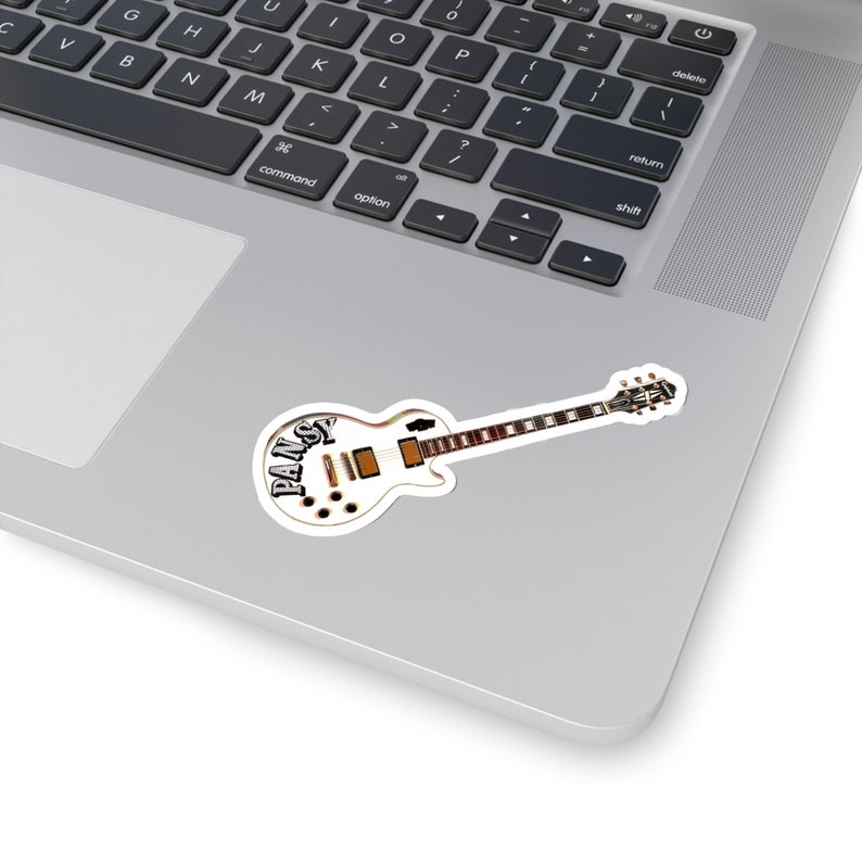 Pode incluir: Uma guitarra el&eacute;trica branca com um design preto e marrom. A guitarra tem a palavra "PANSY" escrita no corpo.