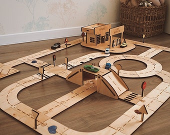 May include: A wooden toy road system with a petrol station and market building, a bridge, a tunnel, traffic signs, and toy cars. The road system is made of interlocking pieces and is designed for children to play with toy cars.