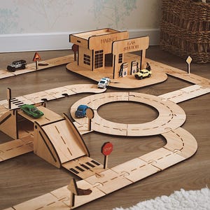 May include: Wooden toy road set with a gas station, market, and various road signs. The set includes a ramp, a roundabout, and several toy cars. The gas station has the text "GAS STATION" and "MARKET".