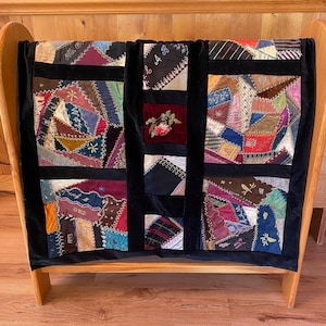 May include: A patchwork quilt featuring a variety of colorful fabric scraps in diverse textures and patterns, joined by decorative embroidery stitches. The quilt is divided by black velvet sashing and includes embroidered letters and floral motifs.