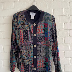 May include: A vintage button-down jacket with a black base and a colorful paisley and geometric pattern. The jacket has long sleeves, a black collar, and decorative gold buttons. The label reads "Lady Carol".