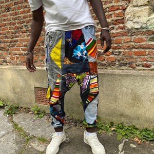 May include: A pair of patchwork trousers featuring a mix of colourful fabrics, including stripes, floral patterns and geometric designs. The trousers are made from denim and have a loose, comfortable fit.