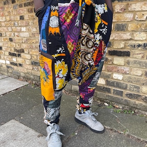 May include: Patchwork trousers with a black waistband and a yellow drawstring. The trousers feature a variety of colourful fabric patches with geometric and floral patterns. The person is wearing grey trainers.