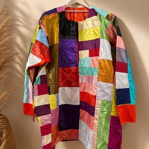 May include: A long-sleeved patchwork jacket in a variety of colours, including red, yellow, purple, and green. The jacket is made of squares of fabric sewn together. The jacket is hanging on a white hanger.