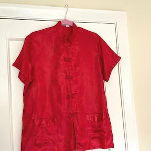 May include: A red silk shirt with a mandarin collar and short sleeves. The shirt has a floral pattern and a button closure.