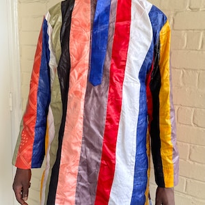 May include: A long-sleeved shirt with vertical stripes in various colours, including red, blue, green, black, white, and pink. The shirt has a round neckline and a button closure.