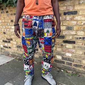 May include: Multi-colored patchwork pants with a variety of patterns, including geometric shapes, palm trees, and African-inspired motifs. The pants are worn with a solid orange t-shirt and gray sneakers.