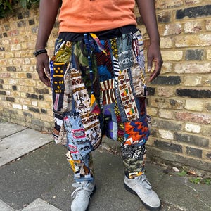 May include: Multi-patterned patchwork trousers featuring a mix of vibrant fabrics with geometric and tribal designs. The trousers have a black waistband and are paired with grey trainers. The style is casual and distinctive, with a unique aesthetic.