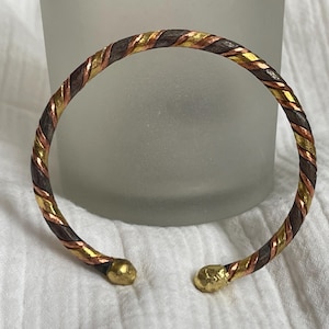 May include: A twisted metal bangle bracelet with copper, gold, and silver tones.