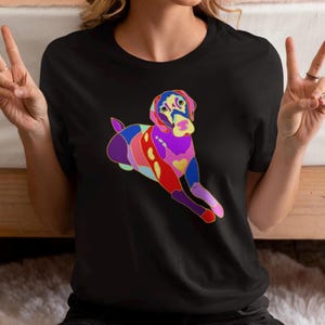 May include: Black t-shirt with a colorful illustration of a dog. The dog is lying down with its head turned to the side. The illustration is made up of different colors, including pink, purple, red, yellow, and blue.