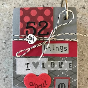 May include: A small gray and red book with a ring binder. The book has a red heart with the word "about" on it, and the text "52 things I love about you".