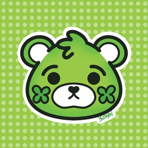 May include: A green cartoon bear with a white outline and black eyes. The bear has a white nose and mouth and two shamrock leaves on its cheeks. The background is a green polka dot pattern.