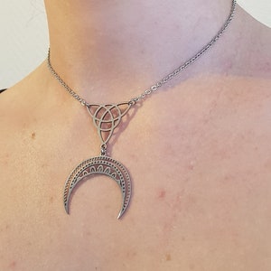 May include: A silver necklace featuring a Celtic knot pendant and a crescent moon charm.